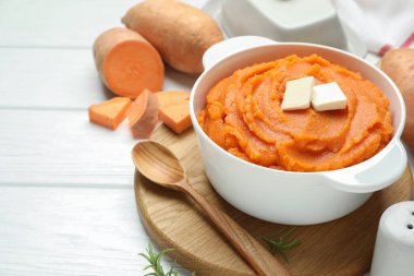 Tatlı patates püresi, tereyağı, kaşık ve taze sebzeler beyaz ahşap masada, yakın plan.