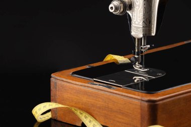 Profesyonel dikiş makinesi ve siyah arkaplanda mezura, yakın plan