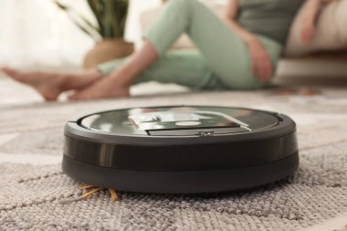Evde dinlenen genç kadın, robotik elektrik süpürgesine odaklan.