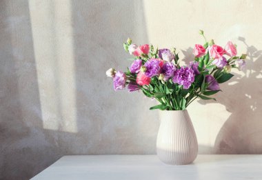 Beyaz ahşap masada güzel Eustoma çiçekleri olan vazo, metin için yer.