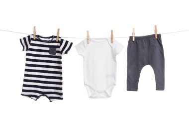 Different baby clothes drying on laundry line against white background