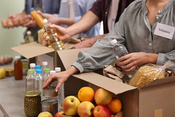 Group of volunteers packing food donations at table indoors, closeup