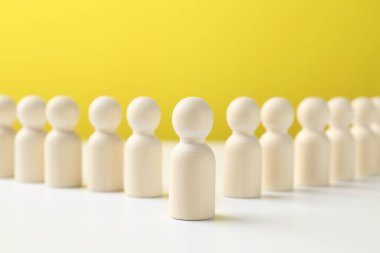 Bir insan figürü, sarı arka plana karşı beyaz masada diğerlerinin arasında duruyor. Rekabet konsepti