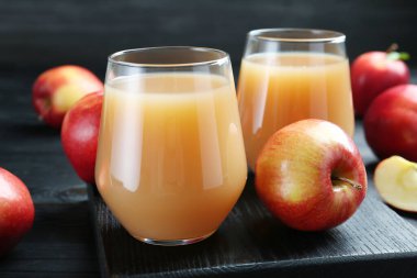 Elma suyunu bardaklarda tazeliyorum ve meyveleri siyah ahşap masada, yakın plan.