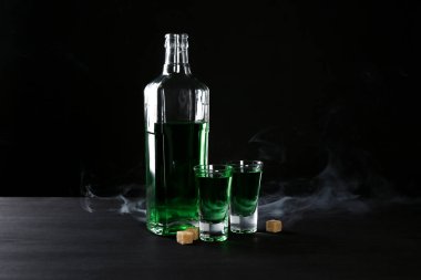 Absinthe shot bardakları, şişe ve esmer şeker siyah arka planda dumanlı