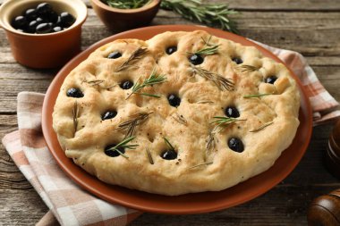 Zeytinli ve biberiyeli lezzetli Focaccia ekmeği ahşap masada, yakın plan.