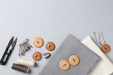 Açık gri arka planda farklı dikiş malzemeleri ve kumaş, düz bir zemin. Metin için boşluk