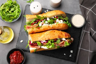 Jambonlu baget sandviç ve kurutulmuş domatesler ve malzemeler gri masada, düzdü.