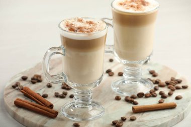 Lezzetli latte macchiato, kahve çekirdekleri ve tarçın çubukları beyaz masada, yakın plan.