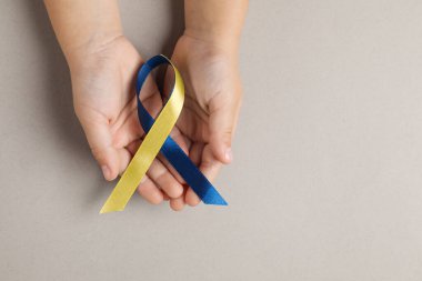 Koyu bej arka planda sarı ve mavi kurdeleli bir çocuk. Down sendromu farkındalığı