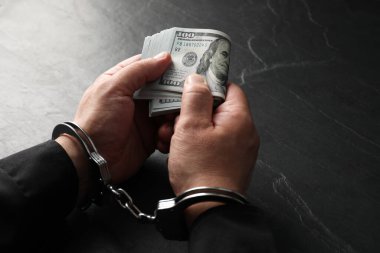 Yozlaşma. Elleri kelepçeli bir adam dolar banknotlarını gri desenli masada tutuyor, yakın plan.