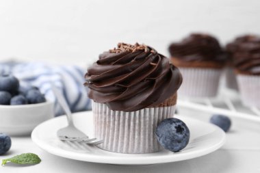 Çikolata kremalı ve yaban mersinli lezzetli kekler beyaz fayanslı masada, yakın plan.