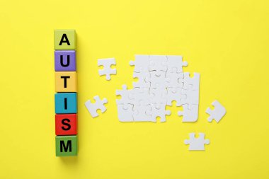 Renkli küplerden ve sarı arkaplanda yapboz parçalarından oluşan kelime otizmi