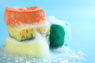 Açık mavi arka planda köpüklü renkli süngerler, yakın plan. Metin için boşluk