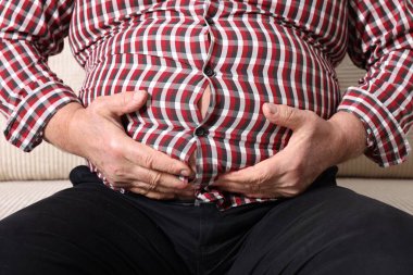 Dar tişörtlü şişman bir adam kanepenin üzerinde, kapalı yerde, yakın plan.