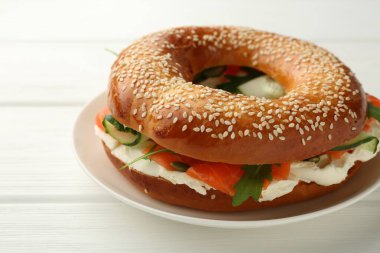 Somonlu leziz simit, krem peynir ve salatalık beyaz ahşap masada, yakın plan.