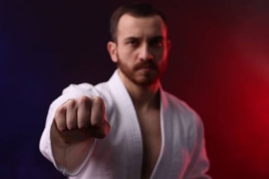 Üniformalı adam renkli ışıklar ve dumanla karate çalışıyor, seçici odaklanma.