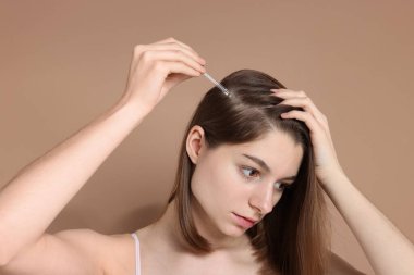 Saç dökülme problemi. Koyu bej arka planda saç çizgisine serum süren kız