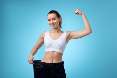 Kilo kaybı. Açık mavi arka planda büyük kot pantolon giyen mutlu kadın.