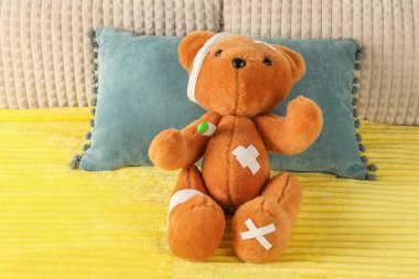 Cute teddy bear with bandages, adhesive medical plasters and thermometer on bed clipart