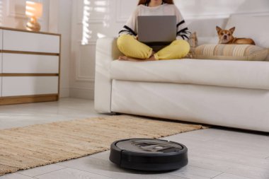 Dizüstü bilgisayarı olan genç bir kız ve evdeki şirin Chihuahua köpeği, robotik elektrik süpürgesine odaklan.
