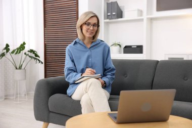 Ofiste dizüstü bilgisayar ve defterle çalışan profesyonel bir psikolog.