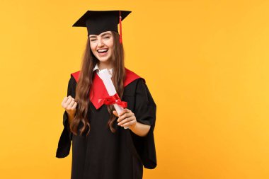 Mezun olduktan sonra turuncu arka planda diploması olan mutlu bir öğrenci. Metin için boşluk