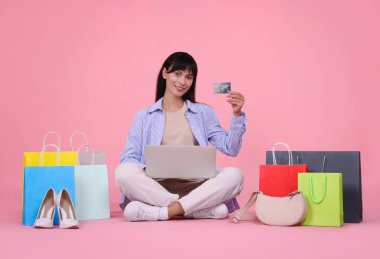 İnternet alışverişi. Kredi kartı, laptop ve pembe arka planda renkli çantaları olan mutlu bir kadın.