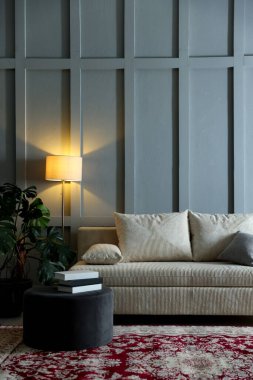 Yastıklı, lambalı, çiçekli rahat bir kanepe ve kapalı alandaki gri duvarın yanında puf. Metin için boşluk