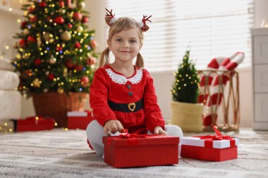 Evde hediye kutularıyla Noel kostümü giymiş küçük kız.