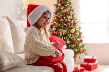 Noel Baba şapkalı küçük kız evdeki kanepede oturuyor.