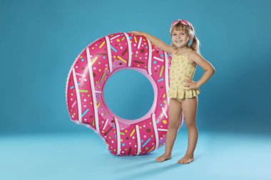 Şişirilebilir yüzüklü, açık mavi arka planda yüzme gözlüklü, mayo giymiş şirin bir kız.