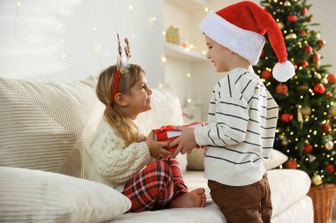 Noel Baba şapkalı küçük mutlu çocuk kız kardeşine Noel hediyesini sunuyor.