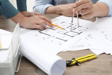 Projeyle çalışan mimarlar, yakın plan. Ahşap masaya farklı teknik çizimler.