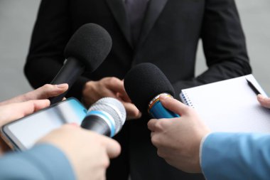Gri arka planda iş kadınıyla röportaj yapan bir grup gazeteci, yakın plan