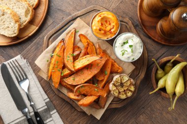 Ahşap masada sosla servis edilen lezzetli pişmiş tatlı patatesler.