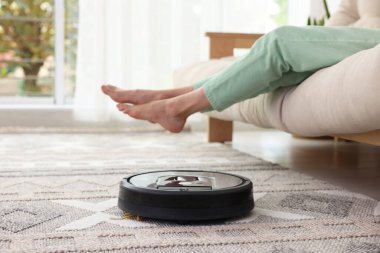 Genç bir kadın kanepede dinlenirken robot elektrikli süpürge evde halıyı süpürüyor, kapanıyor.