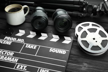 Film alkışı, kamera lensi, film makaraları ve siyah tahta masada bir fincan kahve, yakın plan.