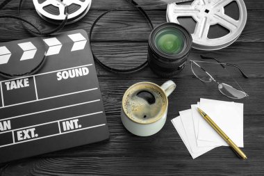 Film alkışı, film makaraları ve kamera lensleri siyah ahşap masanın üstünde.
