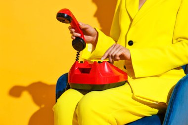 Kırmızı kablolu telefonu mavi koltukta sarı arka planda olan kadın, yakın plan