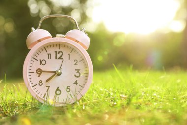 Yeşil çimlerin üzerindeki pembe alarm saati. Metin için boşluk