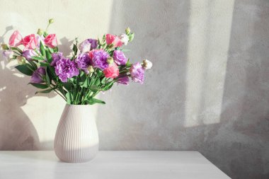 Beyaz ahşap masada güzel Eustoma çiçekleri olan vazo, metin için yer.