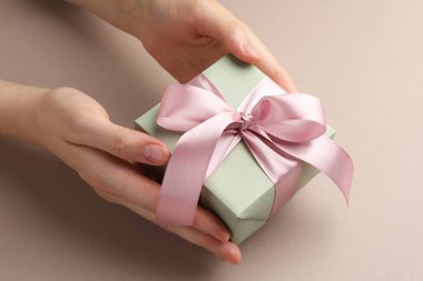 Elinde pembe fiyonklu, bej arka planda hediye kutusu olan kadın, yakın plan.