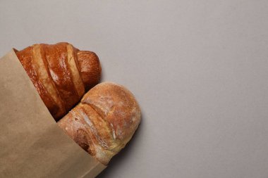 Gri masa üzerinde taze ekmek ve kruvasan bulunan kağıt torba, üst manzara. Metin için boşluk