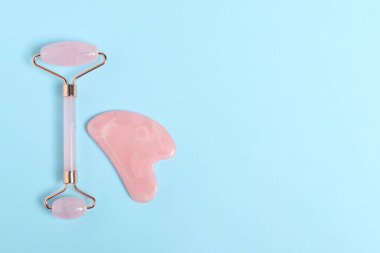 Açık mavi arka planda yüz silindiri ve gua sha aracı, üst görünüm. Metin için boşluk