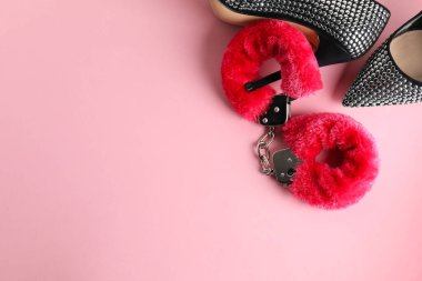Pembe arka planda kabarık kelepçeler ve yüksek topuklu ayakkabılar. Metin için boşluk