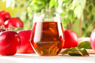 Bardakta taze elma suyu ve dışarıda beyaz masada meyveler, yakın plan.