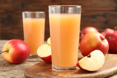 Bardakta lezzetli elma suyu ve ahşap masada taze meyveler, yakın plan.