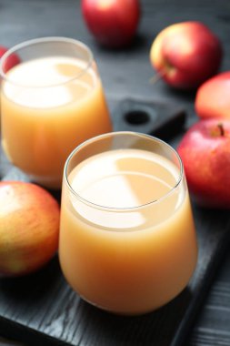 Elma suyunu bardaklarda tazeliyorum ve meyveleri siyah ahşap masada, yakın plan.