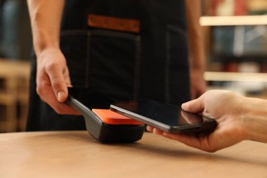 Kafedeki ahşap masada akıllı telefondan ödeme yapan kadın, yakın plan.